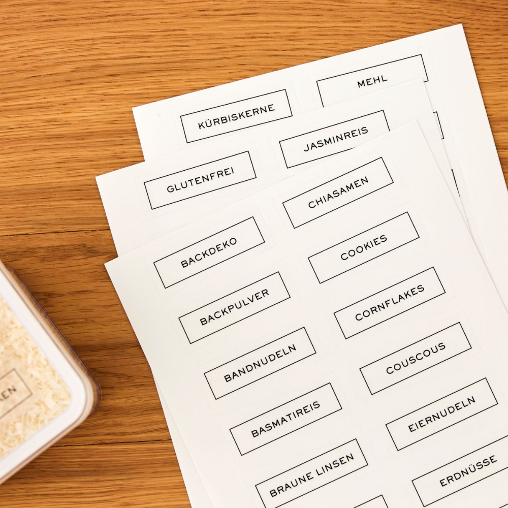 Drei Bögen LOFT Aufkleber - Küchenorganisation von Rotho mit deutschen Lebensmittelnamen wie Kürbiskerne, Mehl und Jasminreis, auf Holz neben Vorratsbehälter - ideal als Etiketten für Trockenvorräte.