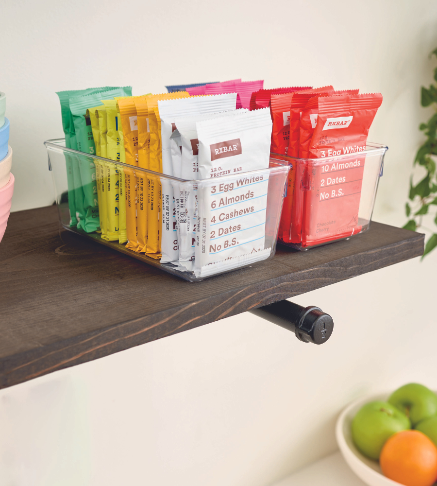 Das Schubladen-Organizer-Set LINUS - HOCH (5-teilig) von iDesign sorgt für Ordnung im Regal neben grünen Äpfeln und Orangen. Die RXBAR-Verpackung stellt die einfachen Zutaten - Eiweiß, Mandeln, Cashews und Datteln - in den Vordergrund.