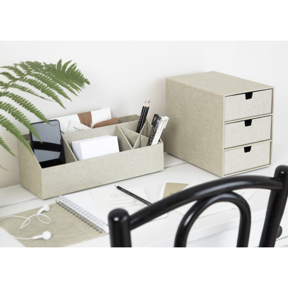 Ein aufgeräumter Schreibtisch mit dem ELISA Schreibtisch Organizer - Linnen Canvas von Bigso in Beige, der Telefon, Briefumschläge, Stifte und Scheren neben einem passenden Schrank mit drei Schubladen aufnimmt. Farnblätter, ein Notizbuch, Kopfhörer und eine Brille ergänzen die aufgeräumte weiße Schreibtischlandschaft.