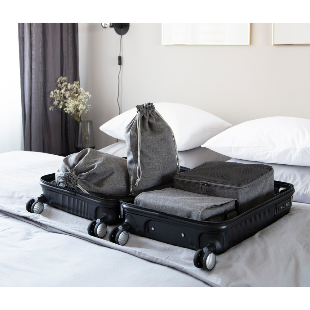 Ein schwarzer Koffer liegt offen auf einem aufgeräumten Bett, gefüllt mit grauen Packwürfeln, Beuteln und dem Bigso TRAVEL Wäschesack Grau - 2 Stk. - ideal für jede Reise. Gedämpftes Licht, weiße Kissen und minimale Dekoration vervollständigen die Szene.