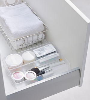 Eine aufgeräumte weiße Schublade mit dem YAMAZAKI TOWER Schubladen Organizer Weiss L (Set 2 Stk.), Metallkorb mit gefalteten Handtüchern und einer durchsichtigen Ablage für Schminkpinsel und Beautyartikel - ideal zum Schubladen organisieren.