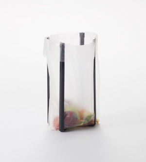 Eine durchsichtige Plastiktüte, die von der YAMAZAKI TOWER Mehrzweckständer Küche - Schwarz, einem eleganten schwarzen Metallständer, offen gehalten wird, zeigt bunte Gegenstände im Inneren vor einem schlichten weißen Hintergrund.