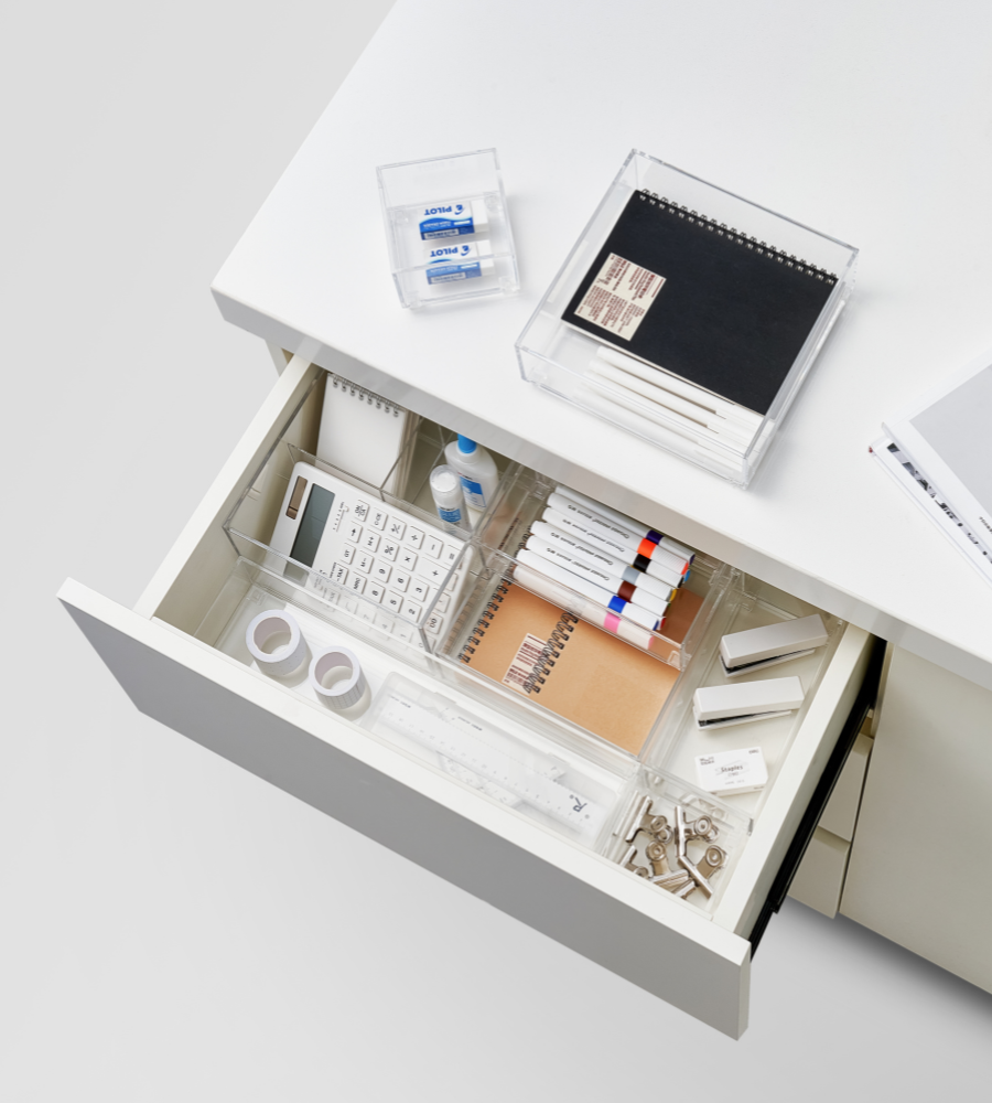 Eine offene Schreibtischschublade nimmt den BNB x VCN SLIDE Schubladen Organizer KLAR - div. Größen, die Stifte, Textmarker, Taschenrechner, Klebeband, Radiergummis, Notizbuch und Klammern ordentlich sortiert; obenauf liegen ein geschlossenes Notizbuch und Radiergummis. Perfekt für Schubladen organisieren.