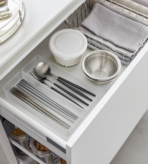 In einer geordneten Küchenschublade sorgt der YAMAZAKI TOWER Schubladen Organizer Weiss L - Set 2 Stk. dafür, dass das Silberbesteck in einem durchsichtigen Tablett neben einem Behälter mit Deckel, einer Metallschüssel und einem Drahtkorb mit gefalteten Stoffservietten oder Tischsets übersichtlich angeordnet ist.