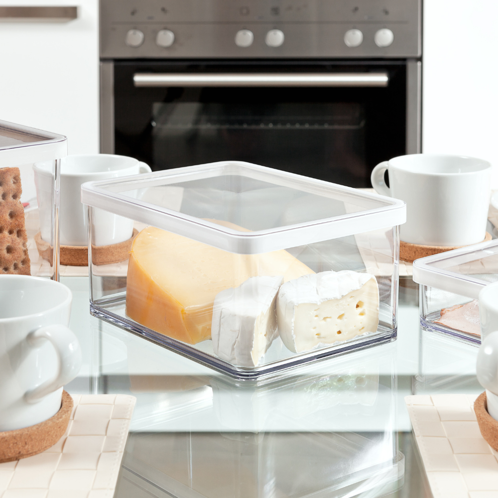 Kunststoffbehälter mit Käse, auf Glastisch mit Tassen in moderner Küche.