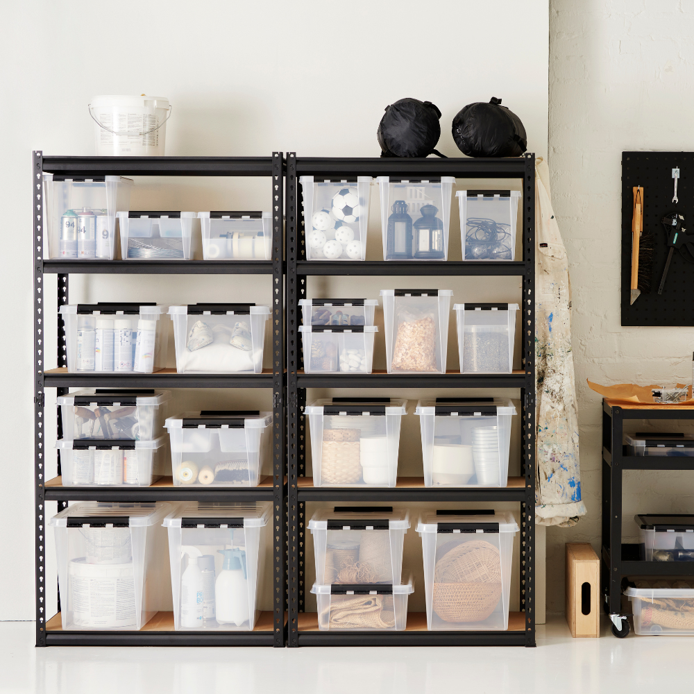 Auf den Metallregalen stehen Orthex SmartStore Box KLAR 40x30x11cm (7,5L), BPA-frei und ordentlich organisiert mit Bastelmaterial. In der Nähe befinden sich eine Arbeitsschürze, eine Stecktafel mit Werkzeugen und ein Rollwagen mit weiteren Materialien.