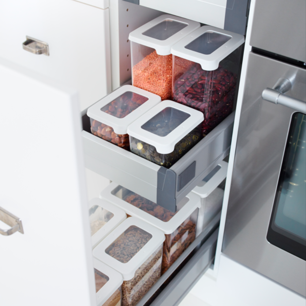 Ein Orthex SmartStore Vorratsdosen KLAR - Weiss Set, jeweils luftdicht verschlossen und gefüllt mit Körnern, Linsen, Bohnen und Nudeln, steht übersichtlich geordnet auf Auszugsböden in einem Küchenschrank neben dem Backofen.
